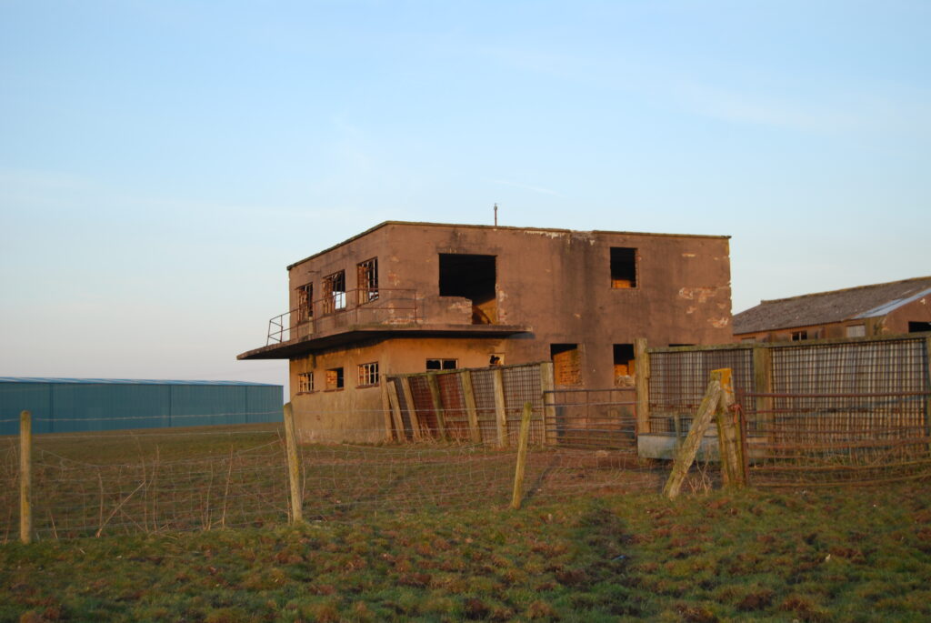 A derelict two storey brick control tower with a balcony to the left hand first floor