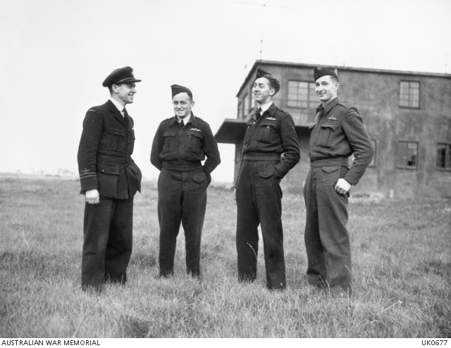 Four uniformed men standing in front of a wartime two storey control tower